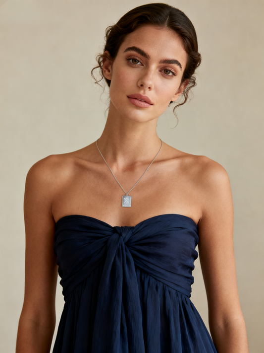 Model wearing Ploutos Jewellery Sagittarius Zodiac Necklace — elegant woman in a navy strapless dress styled with a 925 sterling silver pendant engraved with the Sagittarius symbol and ‘optimistic’ script. Minimalist astrology jewellery from the Cosmic Energy Collection, embodying confidence and adventure.