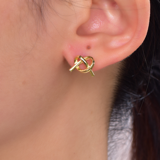 Model wearing 14K gold-plated knot stud earrings from the Abundance Collection — elegant twisted loop design symbolizing unity, love, and abundance, minimalist everyday luxury by Ploutos Jewellery.