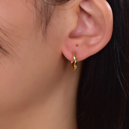 Model wearing 14K gold-plated twisted hoop earrings from the Wealth Collection — small elegant hoops with intertwined design, symbolizing prosperity and grace by Ploutos Jewellery.