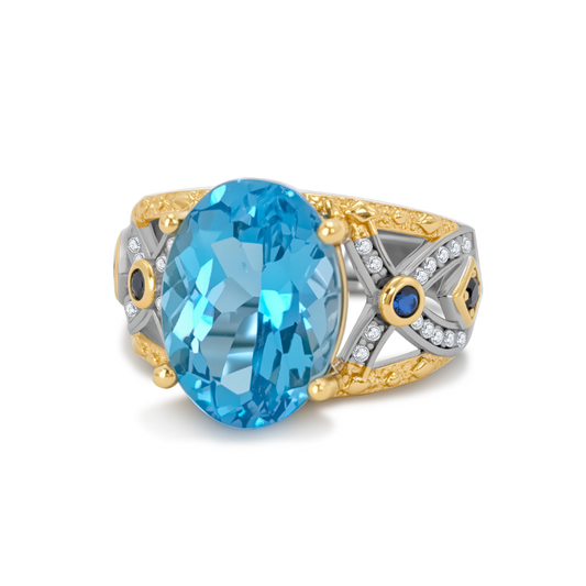 Ploutos Jewellery Azzura Topaz Brilliance Ring — handcrafted 925 sterling silver ring featuring an oval-cut blue topaz with gold-accented details and sapphire-inspired side stones. A statement gemstone ring from the Cosmic Energy Collection symbolising serenity, confidence, and radiant elegance.