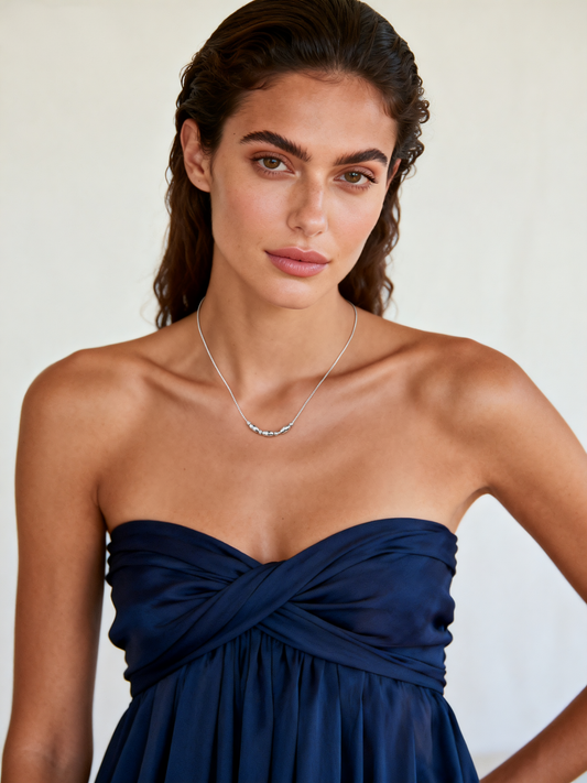 Model wearing Ploutos Jewellery Ethereal Gleam Necklace — a minimalist 925 sterling silver necklace with faceted bead details from the Abundance Collection. Styled with an elegant navy strapless dress, the design reflects refined simplicity, inner confidence, and everyday luxury.