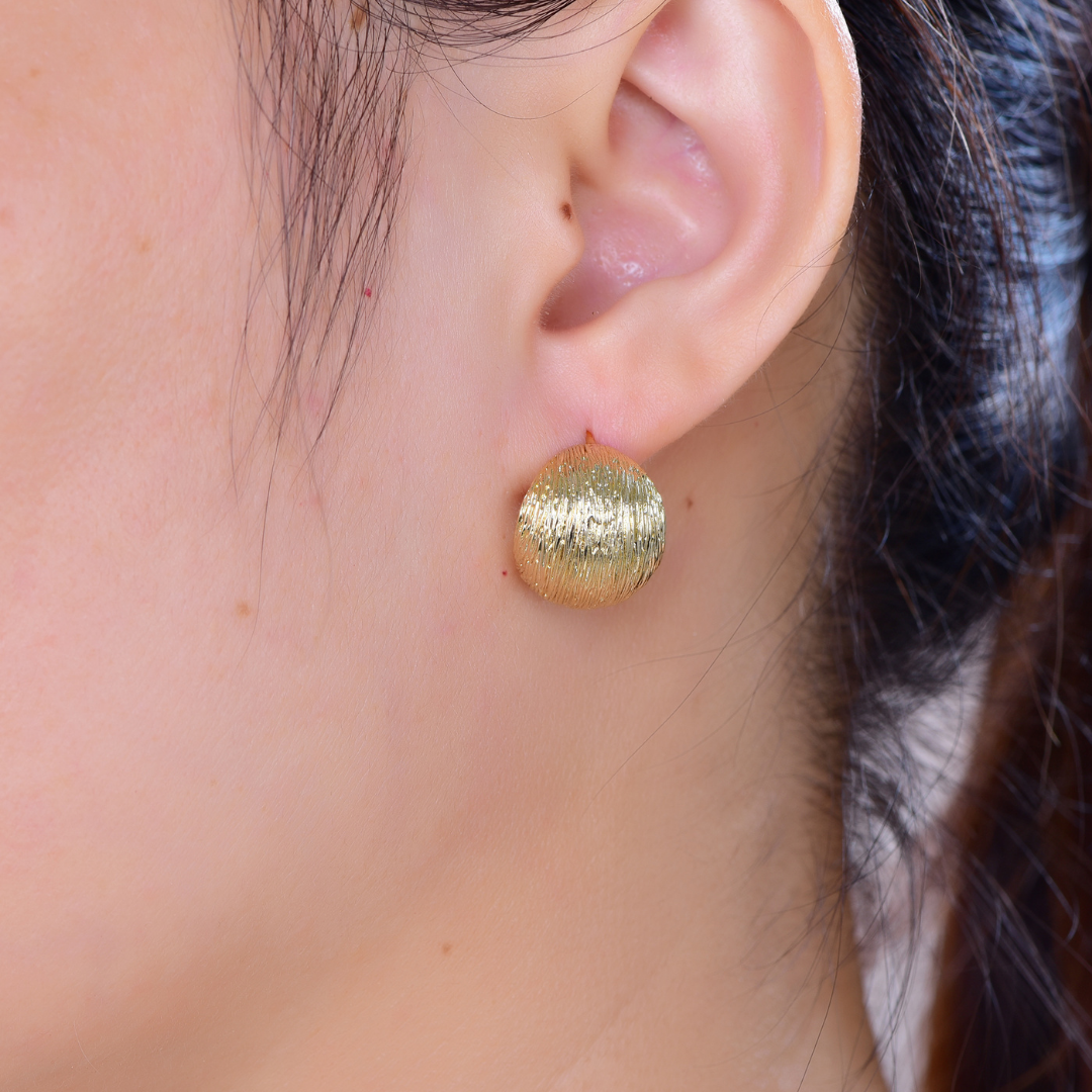 Woman wearing 14K gold-plated round textured dome stud earrings from the Wealth Collection — elegant statement jewellery symbolizing confidence, abundance, and timeless luxury by Ploutos Jewellery.