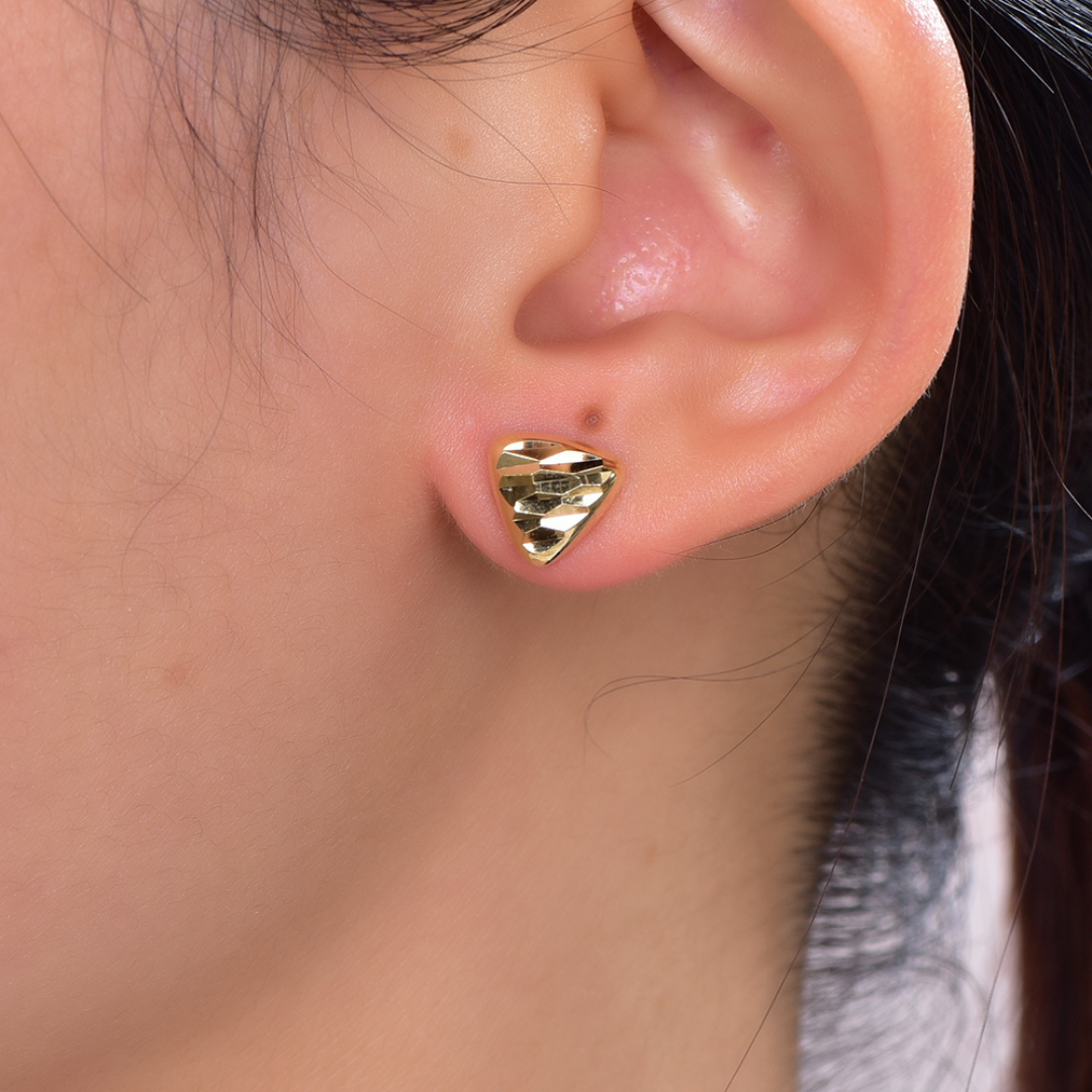 14K gold-plated faceted triangle stud earrings from the Wealth Collection — minimalist geometric gold earrings worn on ear, showcasing reflective facets and timeless quiet luxury by Ploutos Jewellery.