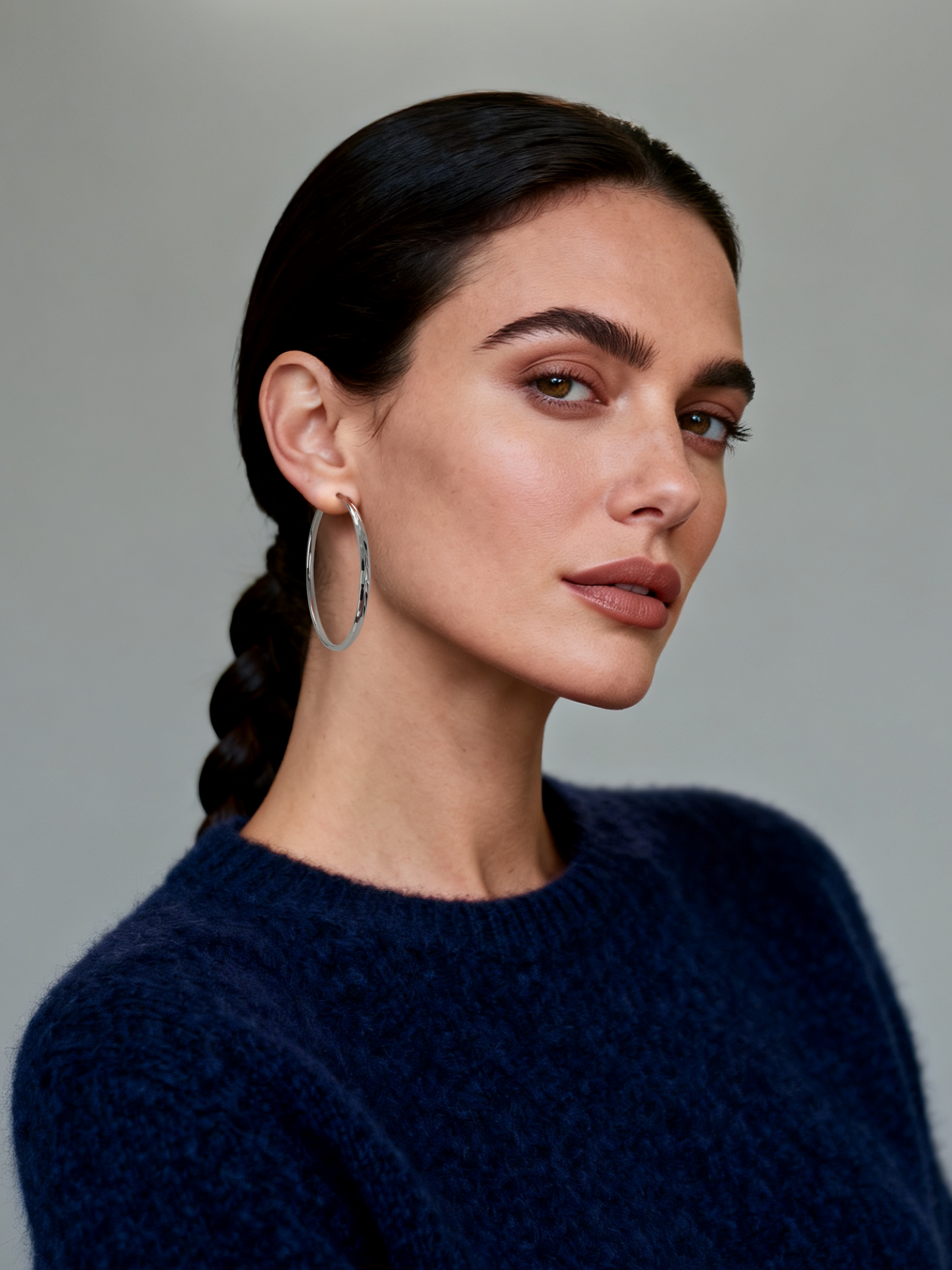 Model wearing Ploutos Jewellery Luna 50mm Faceted Silver Hoop Earrings — 925 sterling silver large hoops with mirror-polished faceted surface, modern minimalist design from the Abundance Collection symbolising elegance, light, and quiet confidence.