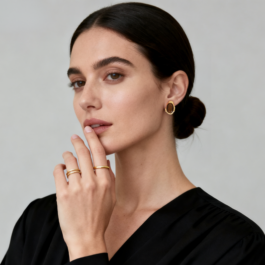 Model wearing Ploutos Jewellery Tiger’s Eye Guardian Studs — 18K gold-plated recycled 925 sterling silver earrings with oval Tiger’s Eye gemstones. The warm golden-brown tones radiate protection and confidence, complemented by minimalist gold stacking rings. A refined look from the Cosmic Energy Collection, blending elegance with grounded strength.